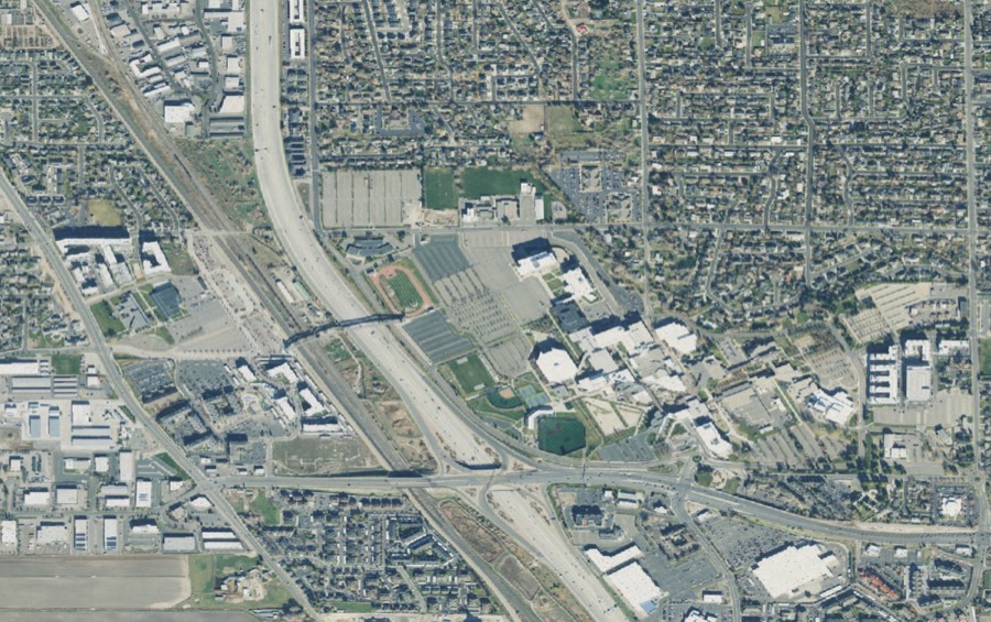 Aerial photograph of the UVU Orem campus: West Campus and the covered pedestrian bridge across I-15 on the left, the academic core at center-right, the new Smith Engineering Building to the east, University Parkway to the south.